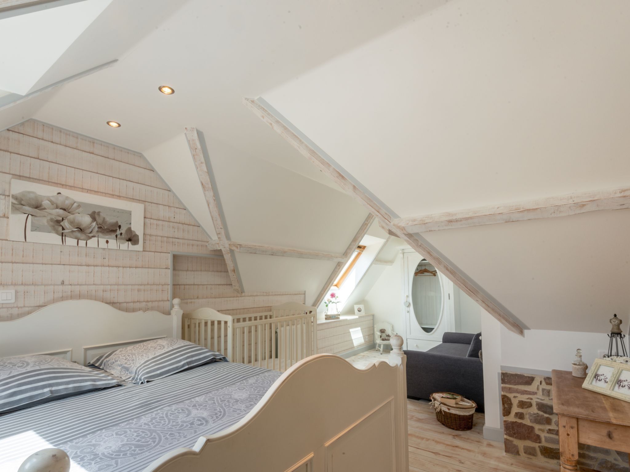 A bedroom with a sloped ceiling, a bed, a dresser, a mirror, and a small table.