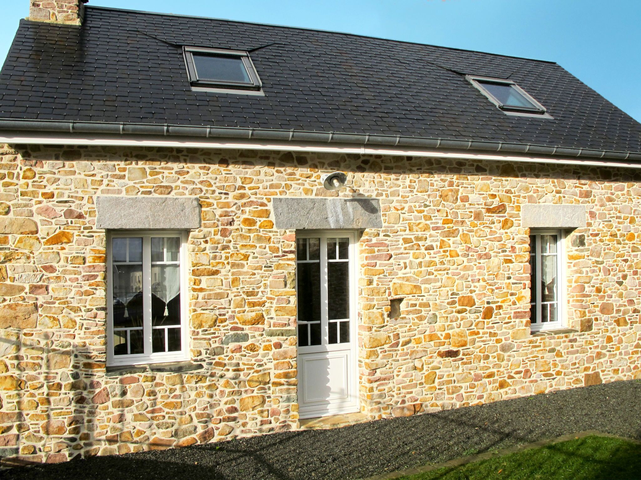 A stone building with three windows, a door, and a small skylight.