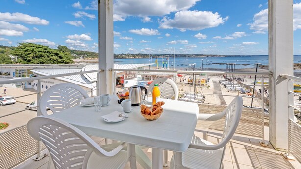 Ein Balkon mit Frühstückstisch, mit Blick auf Strand und Hafen.