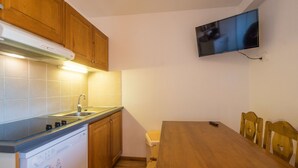 Una cocina compacta con muebles de madera, lavavajillas integrado, una mesa de comedor con sillas y un televisor de pantalla plana montado.
