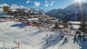 Un centro de esquí cubierto de nieve con varios edificios, pistas de esquí y montañas al fondo.