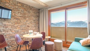 Ein Zimmer mit Steinwand, einem runden Tisch mit Stühlen, einer Couch und einem großen Fenster mit Blick auf die Berge.