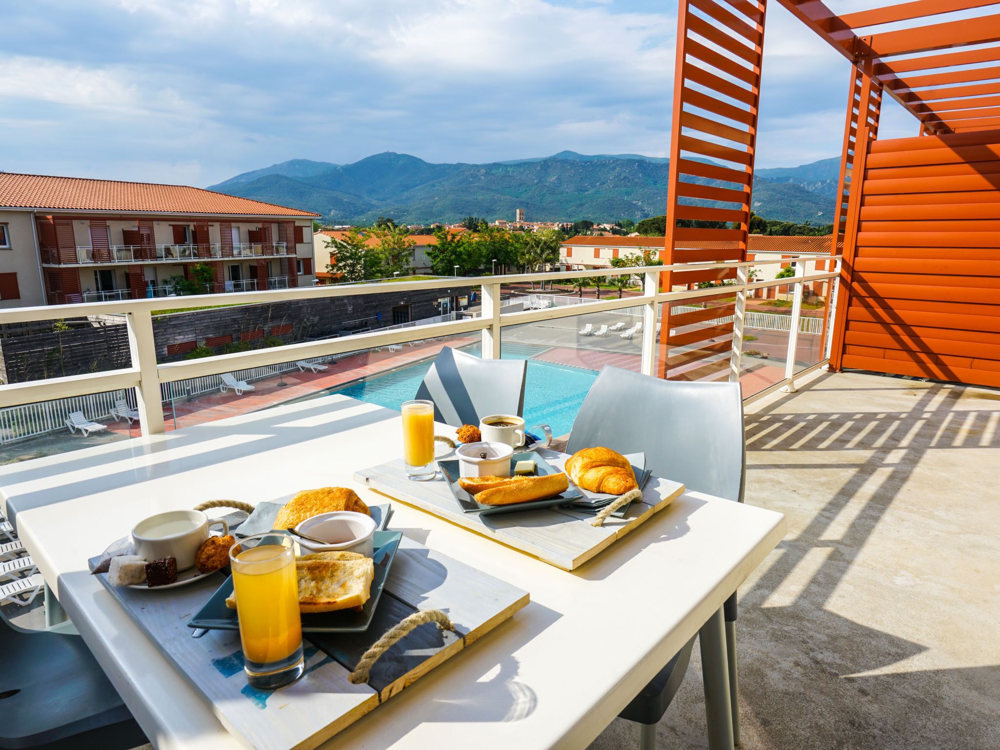 Ein Balkon mit Frühstückstisch, mit Blick auf einen Swimmingpool und Berge.