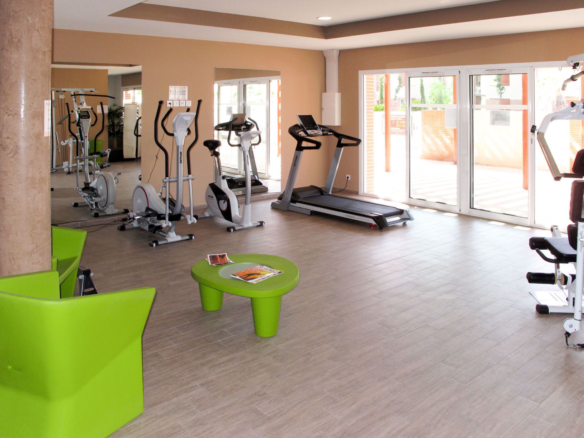 Une salle de sport équipée de divers appareils d’exercice, notamment des tapis de course et des vélos d’appartement, et dotée de chaises vertes vives.