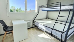 A bunk bed with a desk and chair, a window with a view of trees, and a radiator.