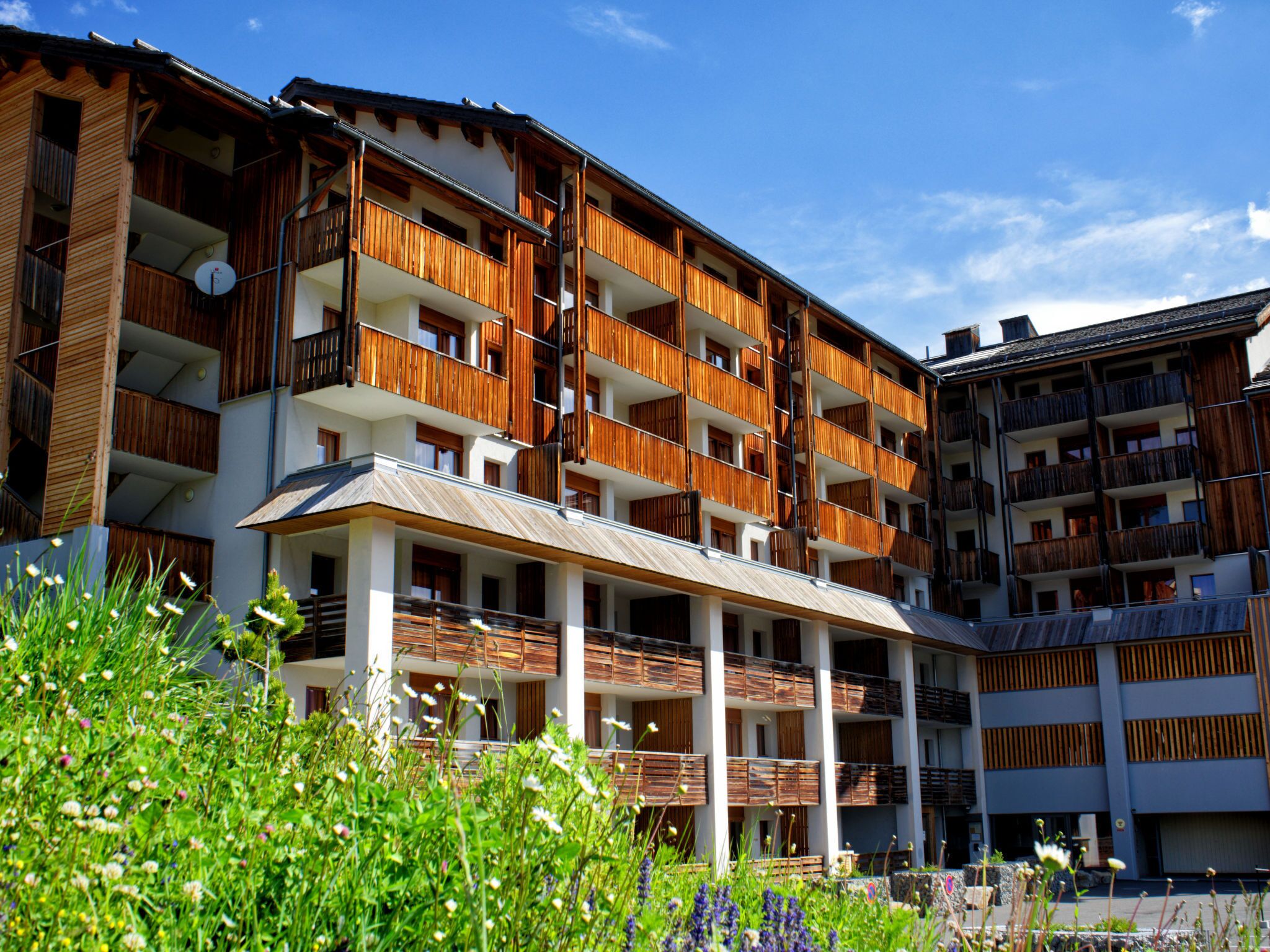 Un hotel de diverses plantes amb balcons de fusta, una zona d'estar exterior coberta i un jardí amb diferents plantes.