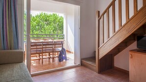 Ein Zimmer mit einer Holztreppe, einer Schiebetür zu einem Außenbereich mit Holztisch und -stühlen sowie einem Sofa.