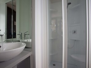Un baño con un lavamanos grande de color blanco, un espejo y una zona de ducha con paredes de vidrio.