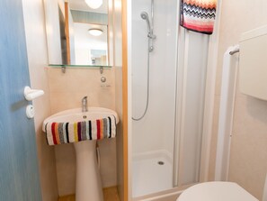 Une salle de bain avec un lavabo blanc, un miroir, une douche et des toilettes.