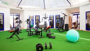 Une salle de sport équipée de divers appareils d’exercice, dotée d’un tapis vert et d’un grand ballon bleu.