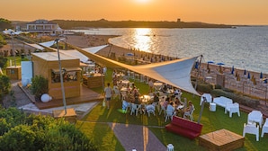 Un espace de restauration en plein air situé en bord de mer, avec des tables et des chaises, une terrasse en bois et une vue sur la mer et le coucher de soleil.