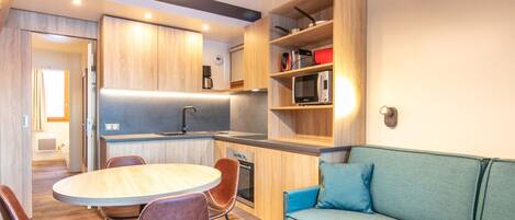 A modern kitchen with wooden cabinets, a dining table with chairs, and a blue sofa.