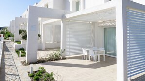 Een modern gebouw met witte buitenmuren, een overdekt terras met witte stoelen en een pad van natuursteen.