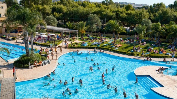 Une grande piscine extérieure entourée d’un espace paysager agrémenté d’arbres et d’un coin salon abrité.