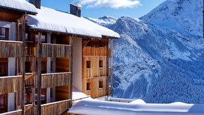 A wooden chalet with a balcony overlooking a snowy mountain landscape.