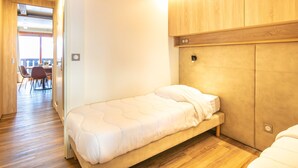Una habitación compacta con una cama individual, cabecera de madera y una pequeña mesa con sillas.