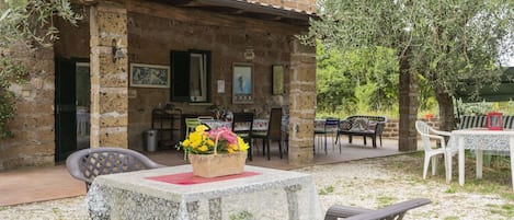 A rustic stone building with a patio area featuring outdoor seating and a table with a floral centerpiece.
