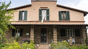 Une maison à deux étages avec une façade en briques, des volets verts et un toit recouvert de tuiles.