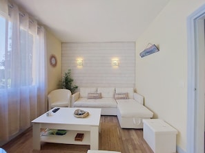 A modern living room with a white sofa, a coffee table, and a small side table. There are two wall-mounted light fixtures and a decorative wall piece.