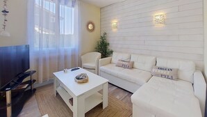 Ein Wohnzimmer mit einem weißen Sofa, einem weißen Couchtisch, einem Fernseher und einer Wandverzierungen.