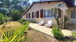 Ein Haus mit Terrasse, weißen Stühlen und einem Garten.