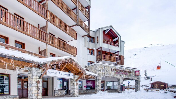 Un edificio de varios pisos con balcones de madera y pilares de piedra, con letreros que indican 'Vacances Le Borsat IV' y 'Lacourandise'.