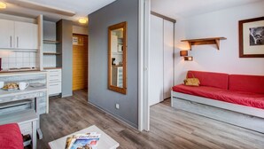 Un espacio habitable compacto con kitchenette, comedor y zona de estar con un sofá rojo.