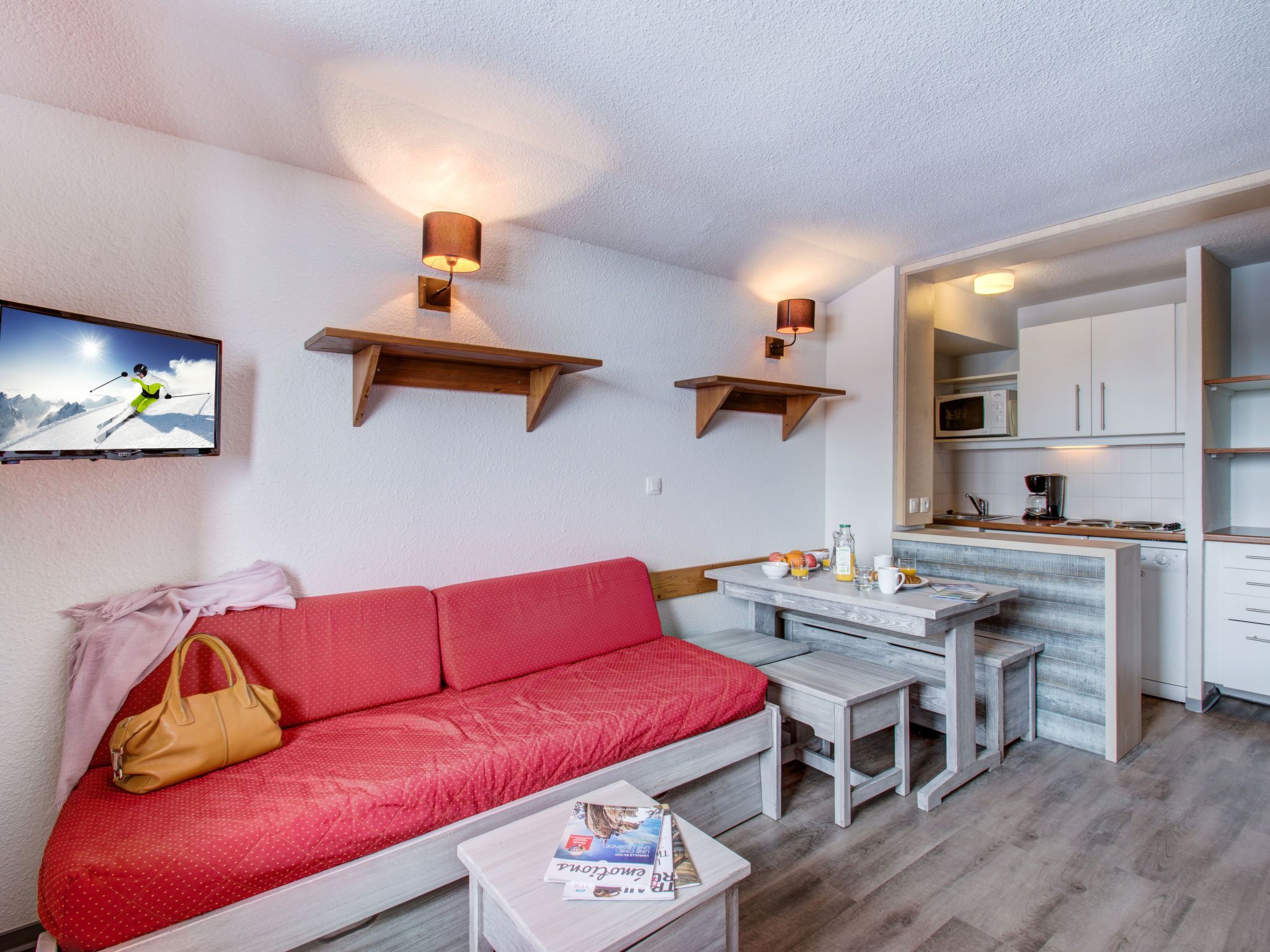 A compact living space with a red sofa, a small dining table, and a kitchen area.