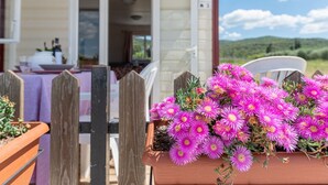 Una terraza de madera con un macetero de flores rosas, una silla blanca y una mesa con mantel morado.