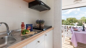 Una cocina moderna con armarios blancos, un lavamanos de acero inoxidable y una encimera de madera. Hay una planta en maceta y una caja de pasta Barilla sobre la encimera.