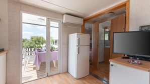 Cocina compacta con refrigerador, televisión de pantalla plana y puerta corrediza de vidrio que da a un patio exterior con mesa y sillas.