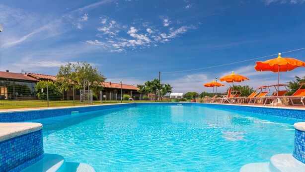 Una piscina azul clara con borde de azulejos, rodeada de sillas de descanso y sombrillas naranjas.