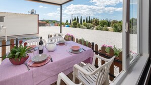 Un patio cubierto con una mesa para dos, con vistas a una zona de grava con vegetación y edificios a lo lejos.