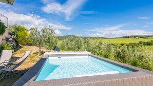 Una piscina rectangular con superficie de agua azul cristalina, rodeada por una terraza de mimbre.