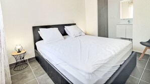 A modern bedroom with a bed, a bedside table with a lamp, and a bathroom visible through an open door.