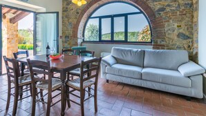 A dining area with a stone wall, a large arched window, and a sofa.