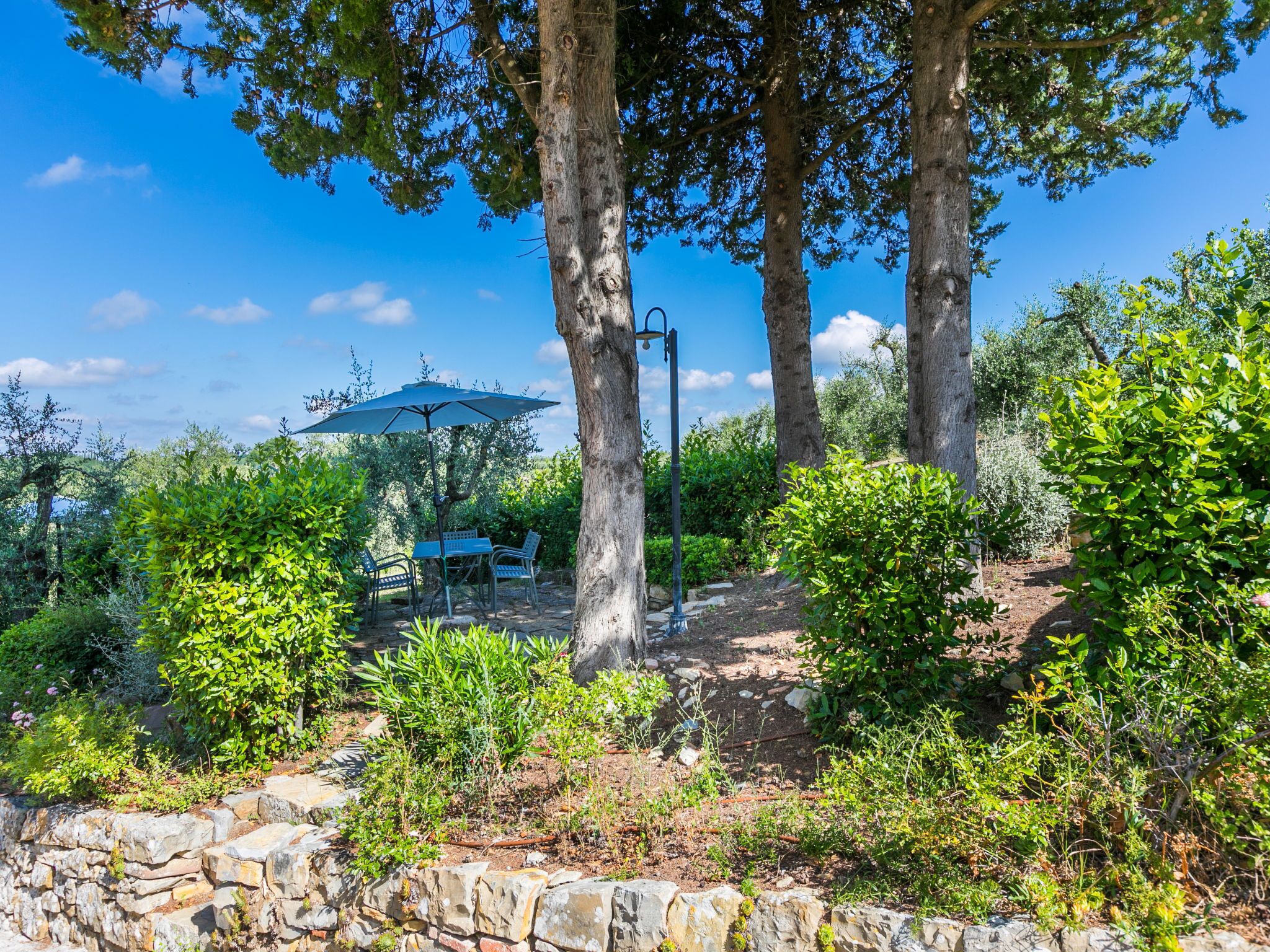 Eine Terrasse mit Steinmauern, einem Tisch, Stühlen und einem Sonnenschirm.