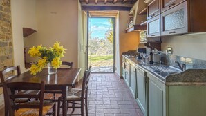 Une cuisine avec des meubles en bois, une table à manger avec des chaises et une vue sur l’extérieur.