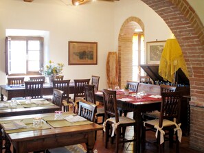 A dining area with wooden tables and chairs, a piano, and a brick wall. - Antico Borgo San Lorenzo by Interhome (Colle Val d'Elsa)