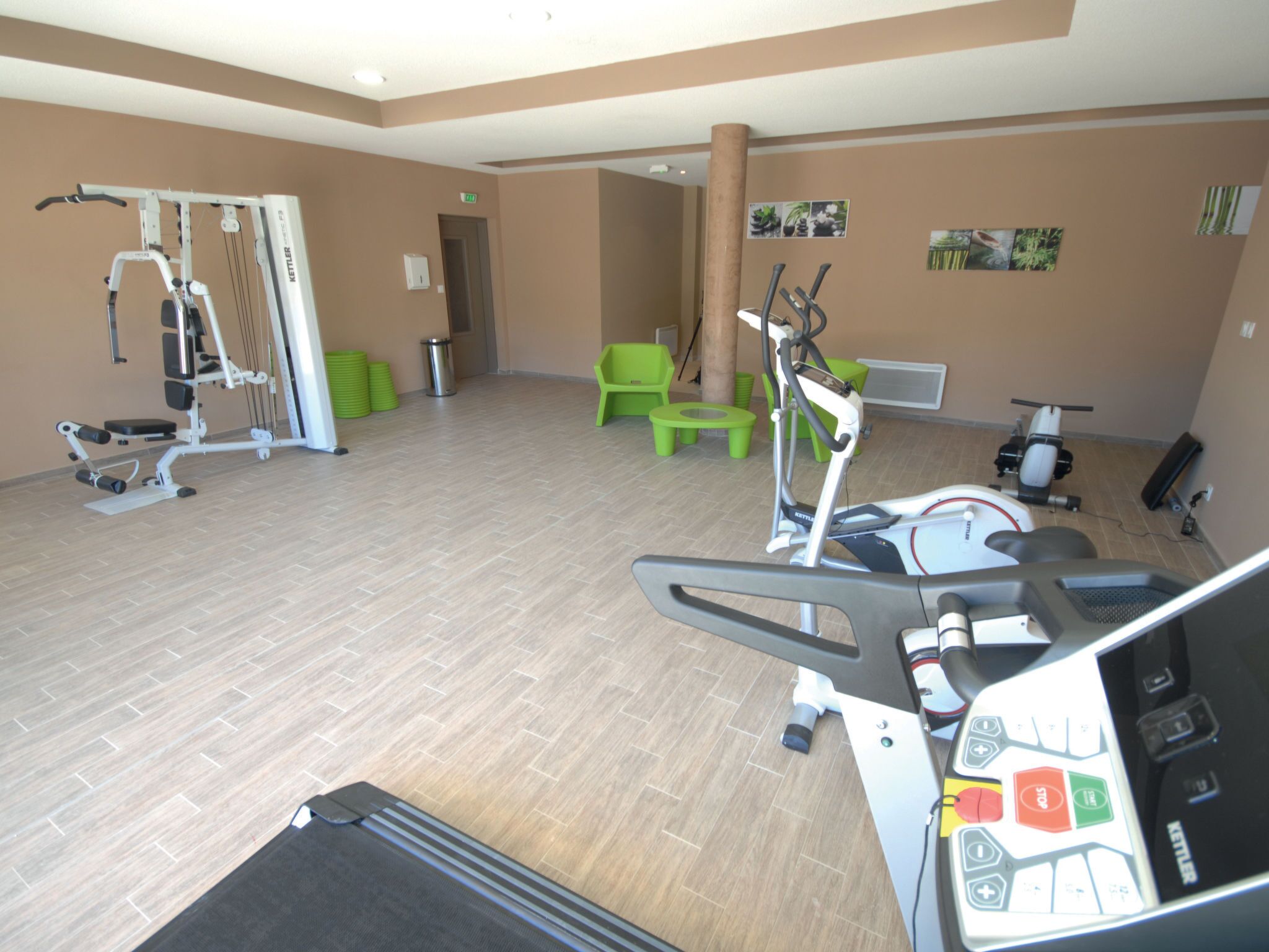 Un gimnasio con equipamiento de ejercicio, sillas verdes y una pared con fotografías.