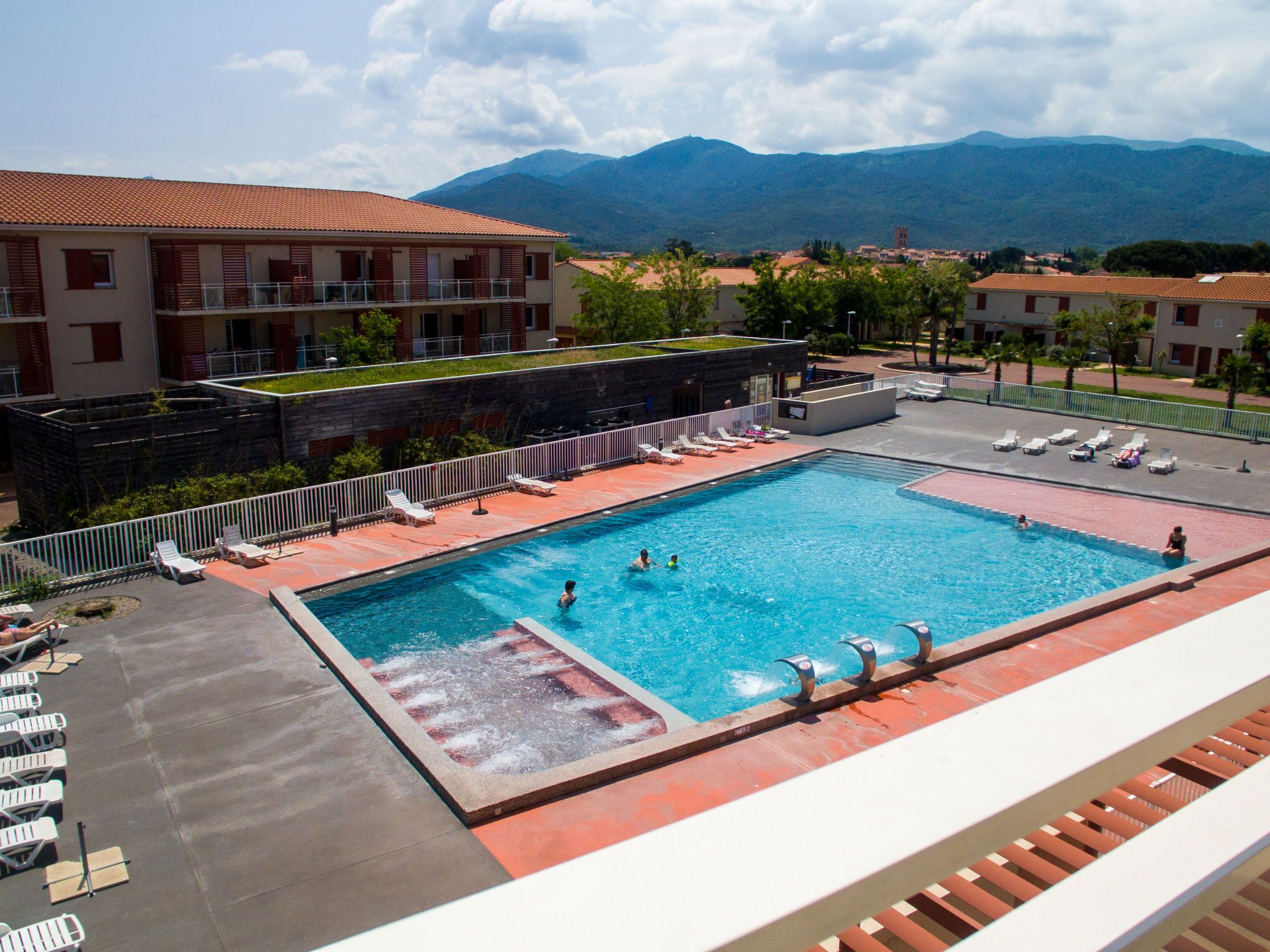 A swimming pool with multiple lanes, surrounded by lounge chairs and a view of mountains in the background.