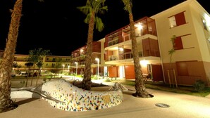 Un hotel de varios pisos con balcones, una piscina con baldosas y palmeras.
