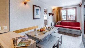 Una cocina moderna con una mesa de madera, bancos y un sofá rojo. Hay cuadros en la pared y una ventana con cortinas.