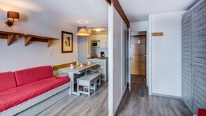 Un espacio habitable compacto con un sofá rojo, una mesa de comedor con bancos, una kitchenette y una puerta de madera.