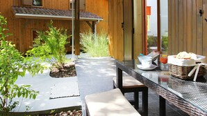 Eine Holzhütte mit einer Terrassenfläche, komplett mit Tisch, Frühstücksutensilien, einer Bank und Blick auf die umliegende Natur.