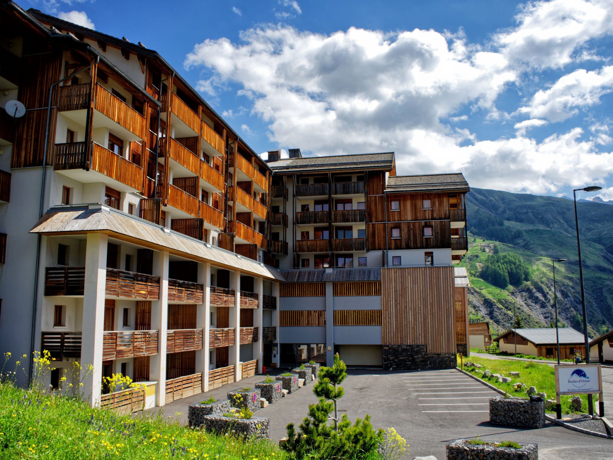 A multi-story hotel with wooden balconies and a parking area.