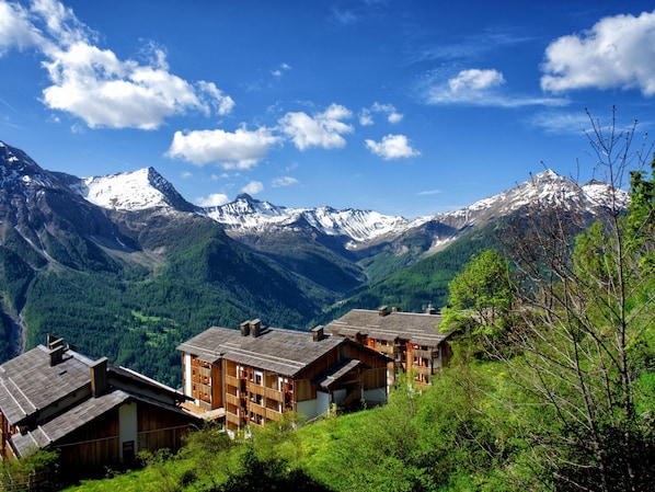 Un village de montagne aux maisons en bois, une vallée et, au loin, des sommets enneigés.