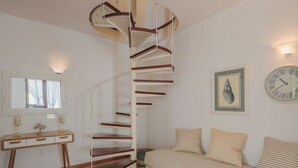 A spiral staircase with wooden steps and white railings, a bed with striped pillows, a bedside table with a lamp, a framed picture on the wall, and a clock. - Vacation home Rosa by Interhome (Lido di Camaiore)