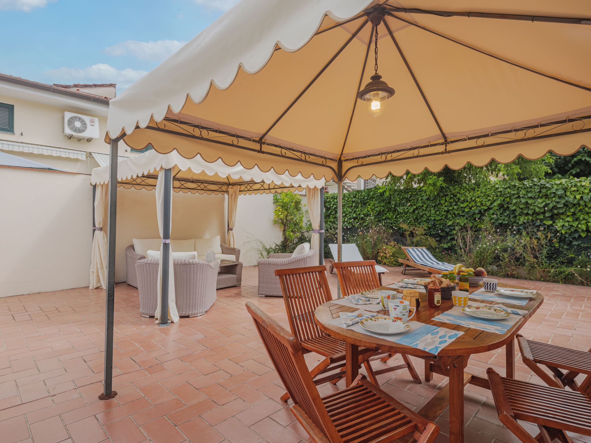 A covered outdoor patio with a table set for dining, wicker furniture, and a hanging light fixture.