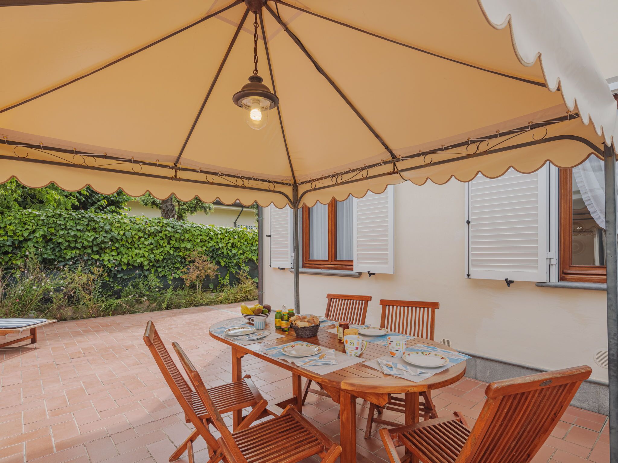 A covered patio with a table set for dining, surrounded by chairs, and a hanging light fixture.